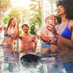 DOTBEATS Mini Wireless Bluetooth Speaker, Black, Floating on water, with a group of friends partying in the pool.