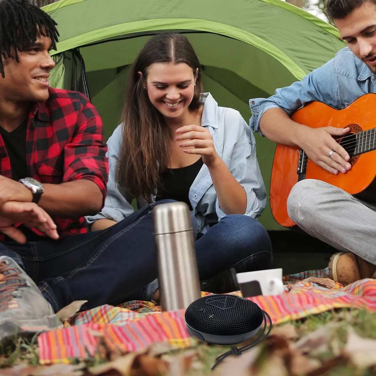 DOTBEATS Mini Wireless Bluetooth Speaker, Black,  sits atop a mat, encircled by three campers